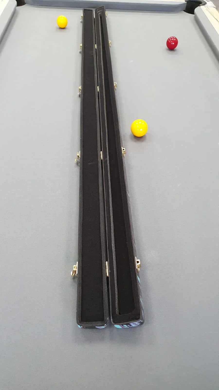 Open cue case on a grey pool table with red and yellow pool balls