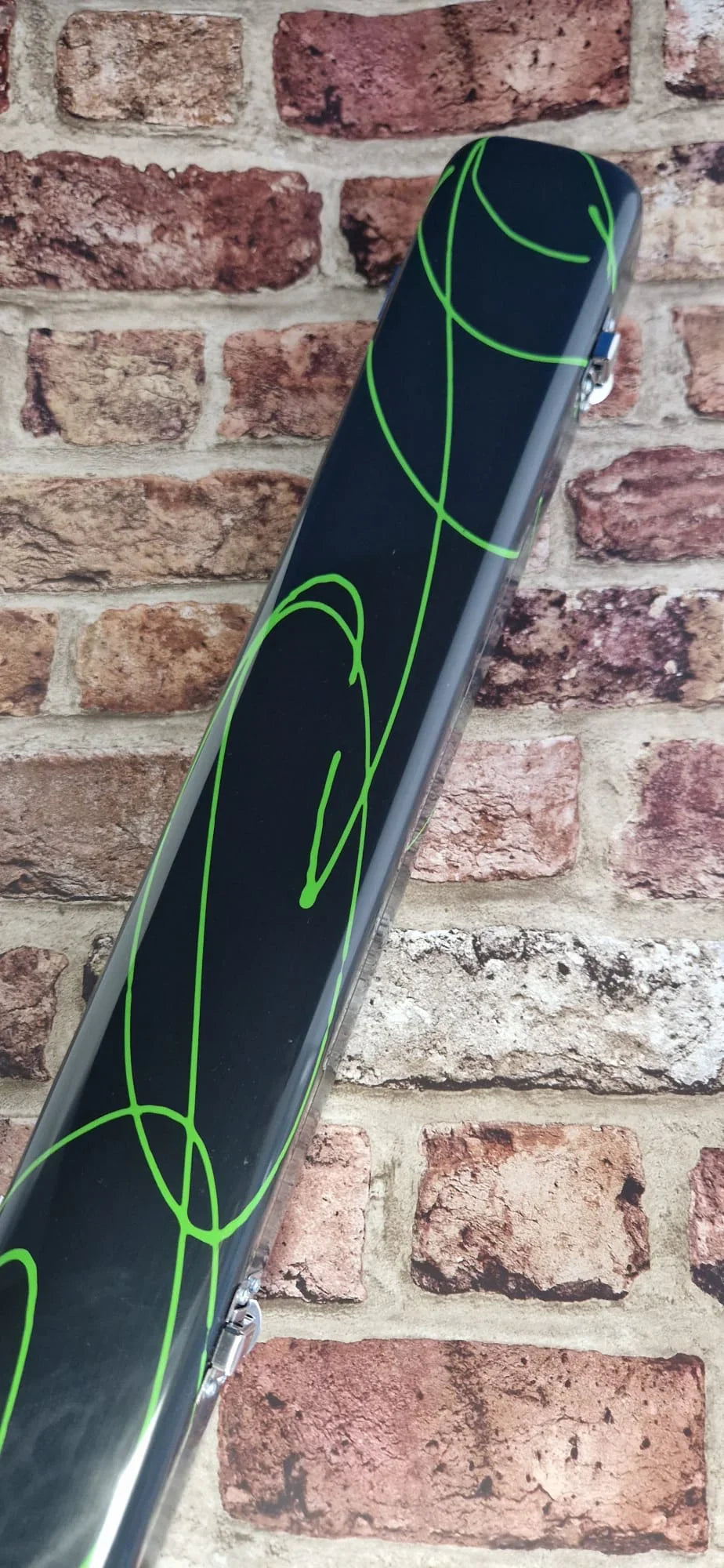 Black hard case with green abstract lines against brick wall background