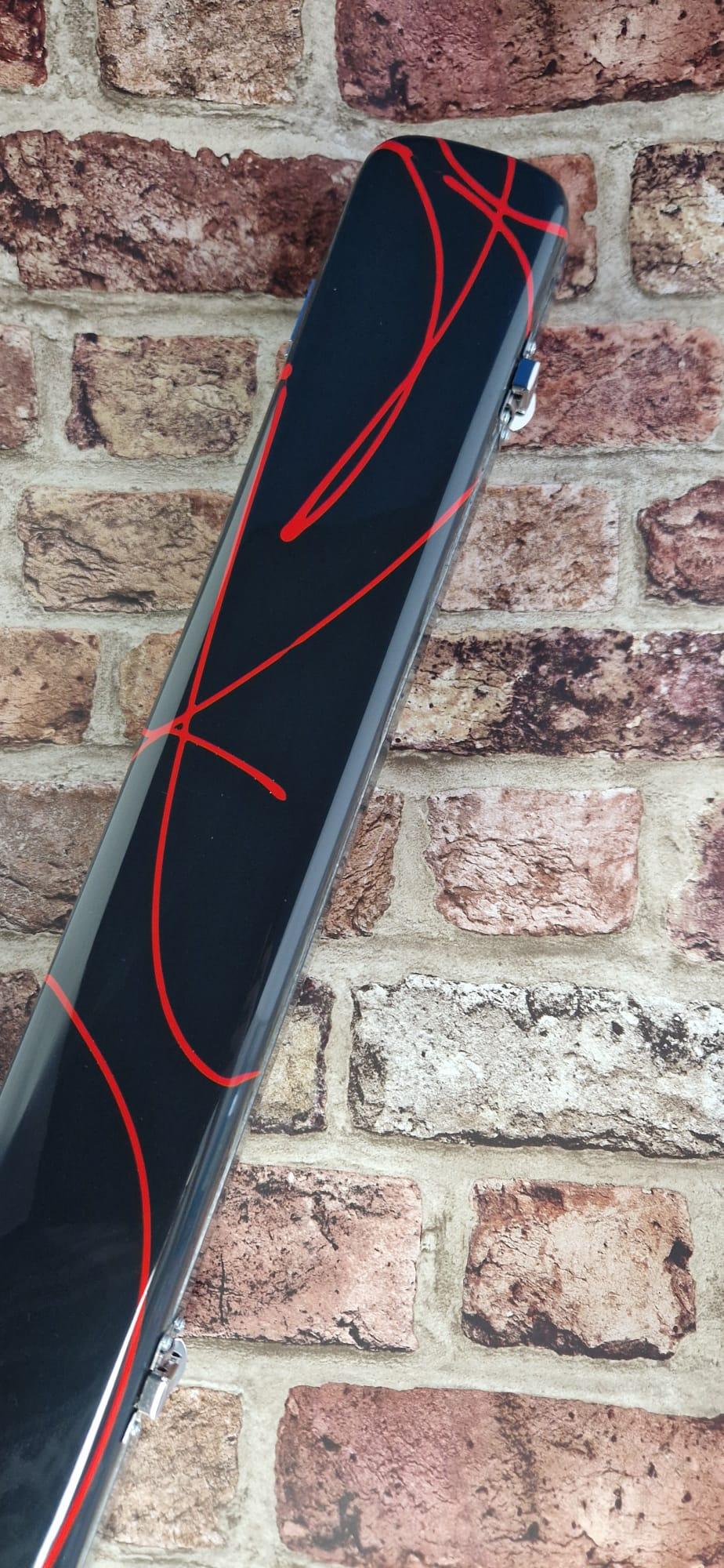 Black hard case with red abstract lines and silver clasps against a brick wall background