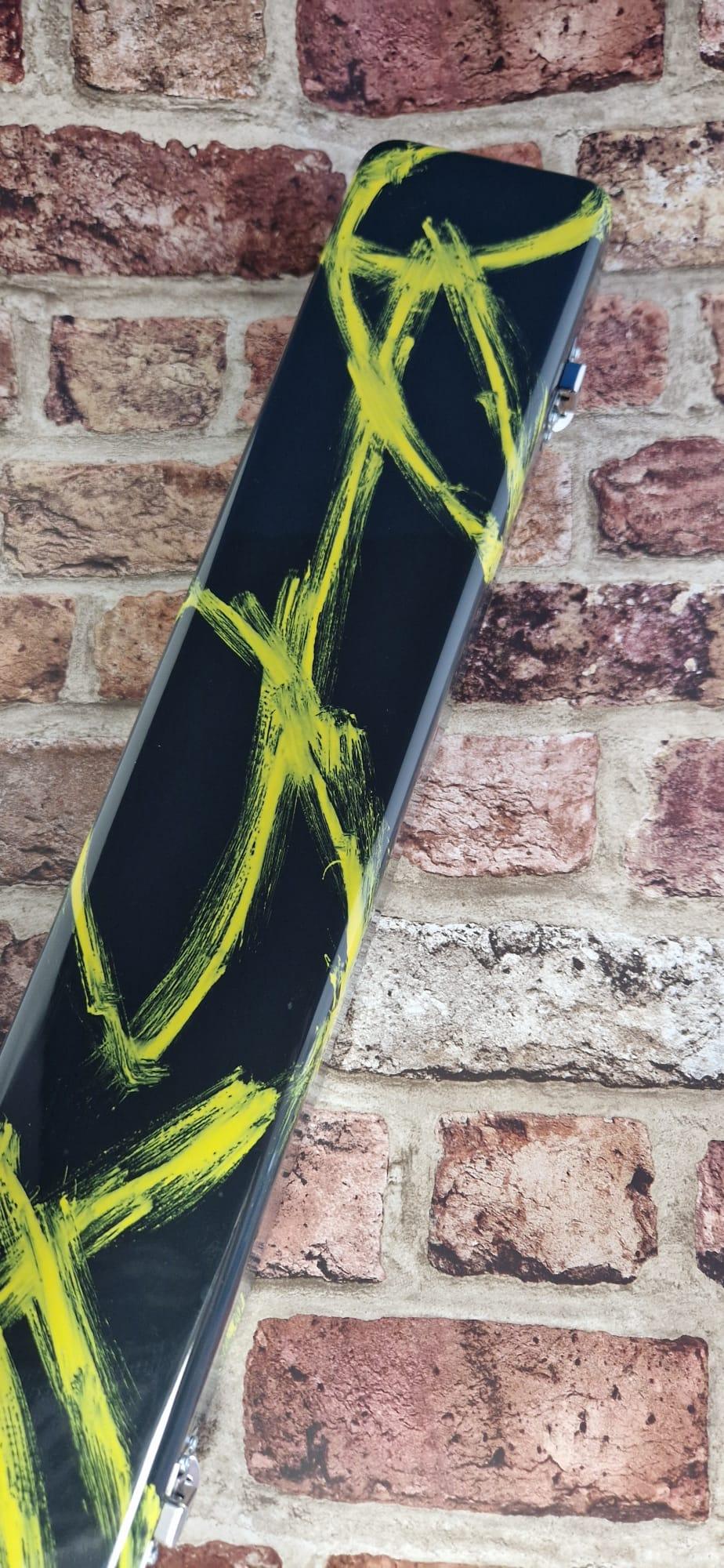 Black guitar case with yellow abstract paint on brick wall background