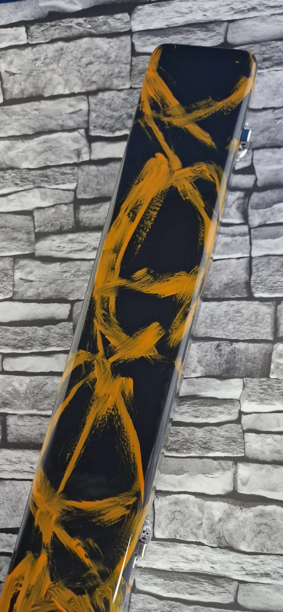 Black hard case with bold yellow paint strokes, stone brick wall background