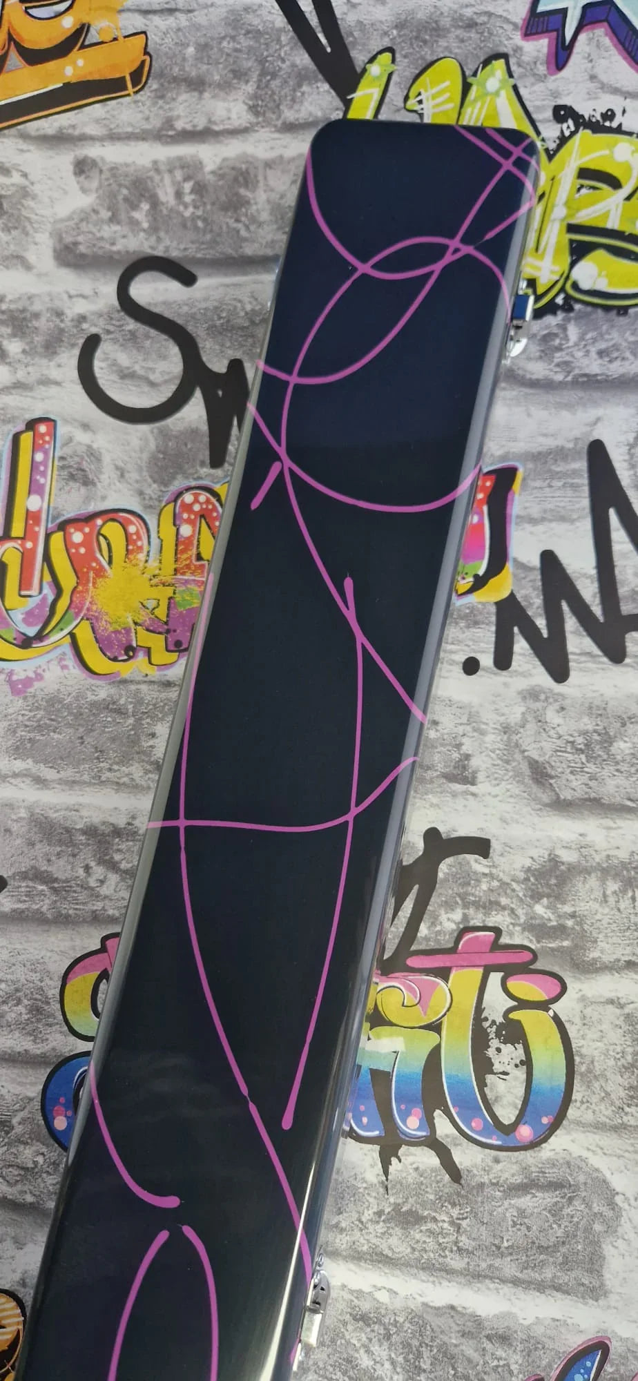 Black rectangular case with pink abstract lines on graffiti brick wall background